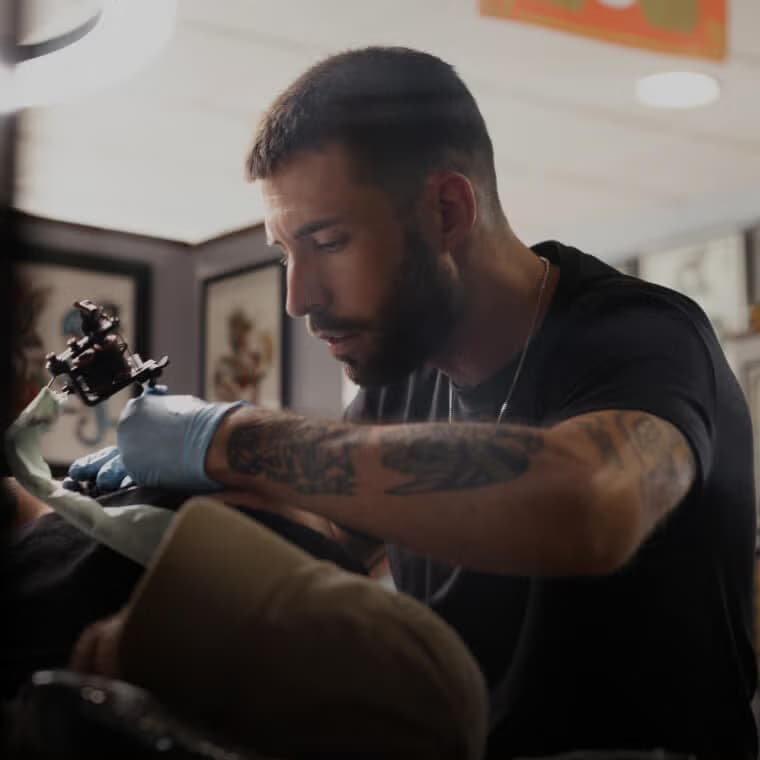 Tatoeëerder die een gedetailleerd ontwerp maakt op de arm van een klant in een studio, ter illustratie van tatoeage- en piercingservices op Salony.