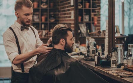 Kapper die de baard van een klant trimt met een tondeuse in een kappersstoel