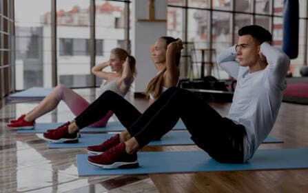 Drie mensen die samen sit-ups uitvoeren op matten in een fitnessstudio