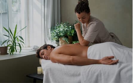 Massagetherapeut die een rugmassage geeft aan een klant die op een behandeltafel ligt