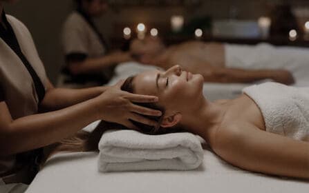 Vrouw die ontspant met haar ogen dicht terwijl ze een witte badjas en hoofddoek draagt in een spa-omgeving